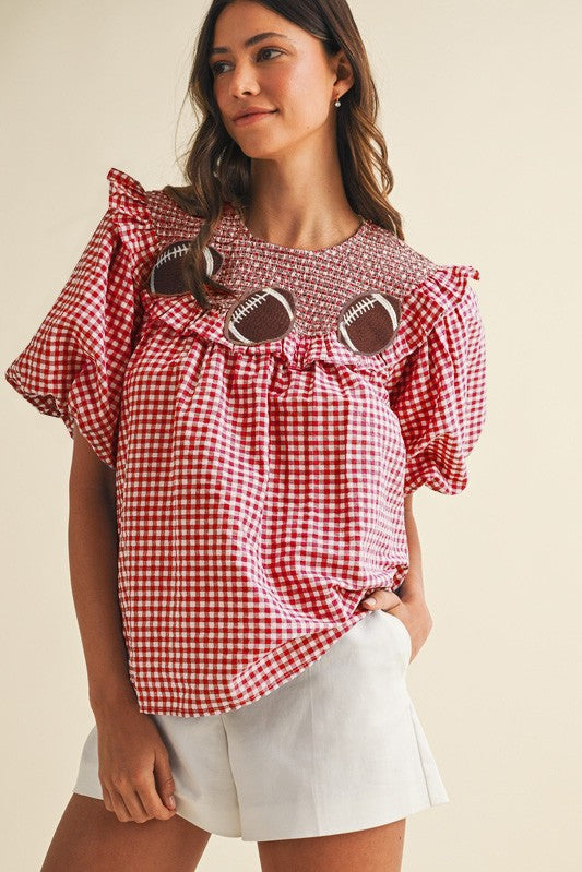 Woman wearing a red and white checkered blouse with puff sleeves on a beige background