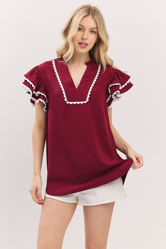 Woman wearing a burgundy top with ruffled details on a white background