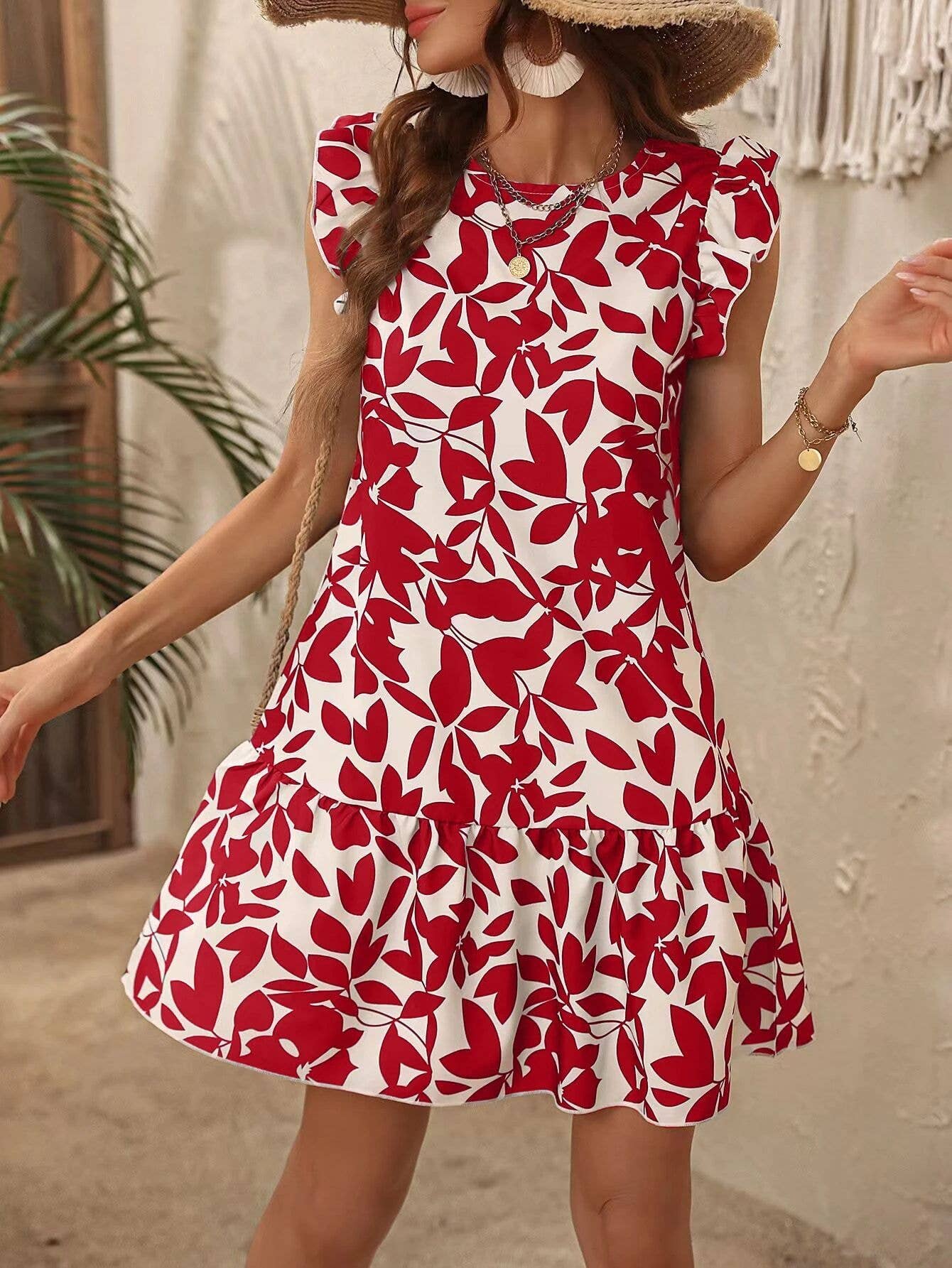 Woman wearing a red and white floral dress with a straw hat in an outdoor setting.