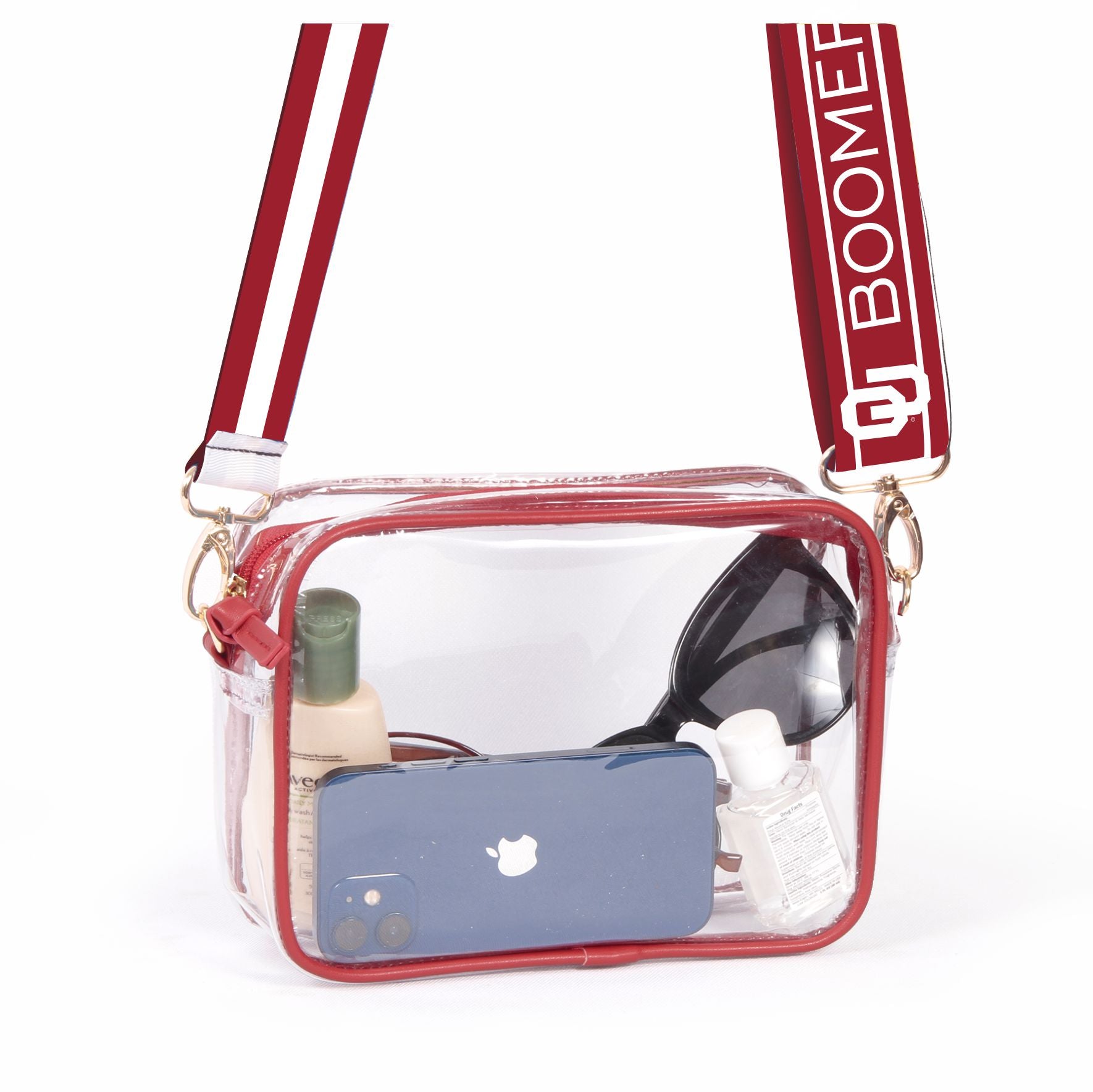 A clear vinyl purse with red vegan leather trim and brass hardware. The purse has a red shoulder strap with white text 'BOOMER' and is displayed with various contents visible through the clear material.