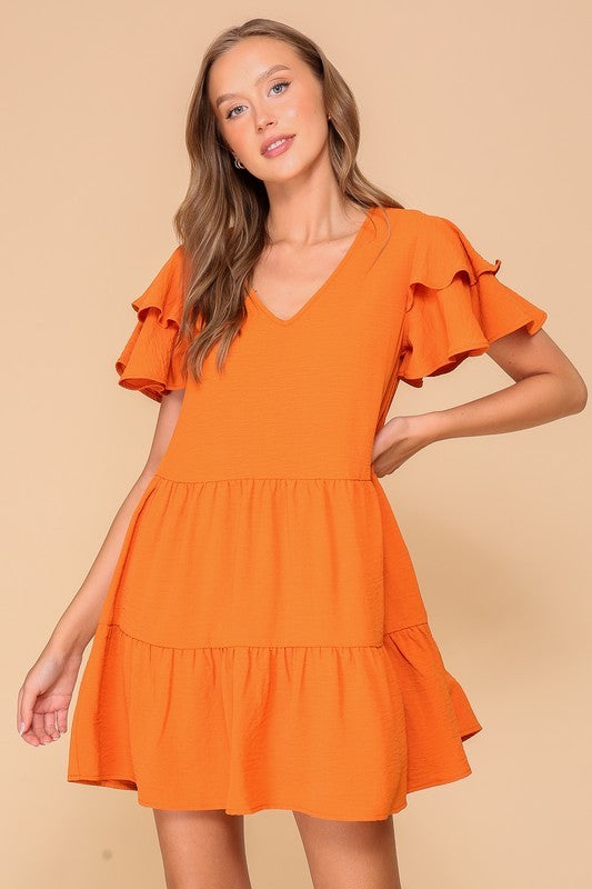 Woman wearing an orange dress with ruffled sleeves against a beige background
